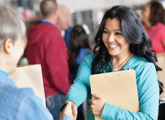 Woman with dark hair smiles as she shakes hands with another person at a job fair.